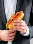 16330398-business-man-in-suit-holding-his-lunch-baguette-sandwich-roll-with-bacon-lettuce-and-tomato